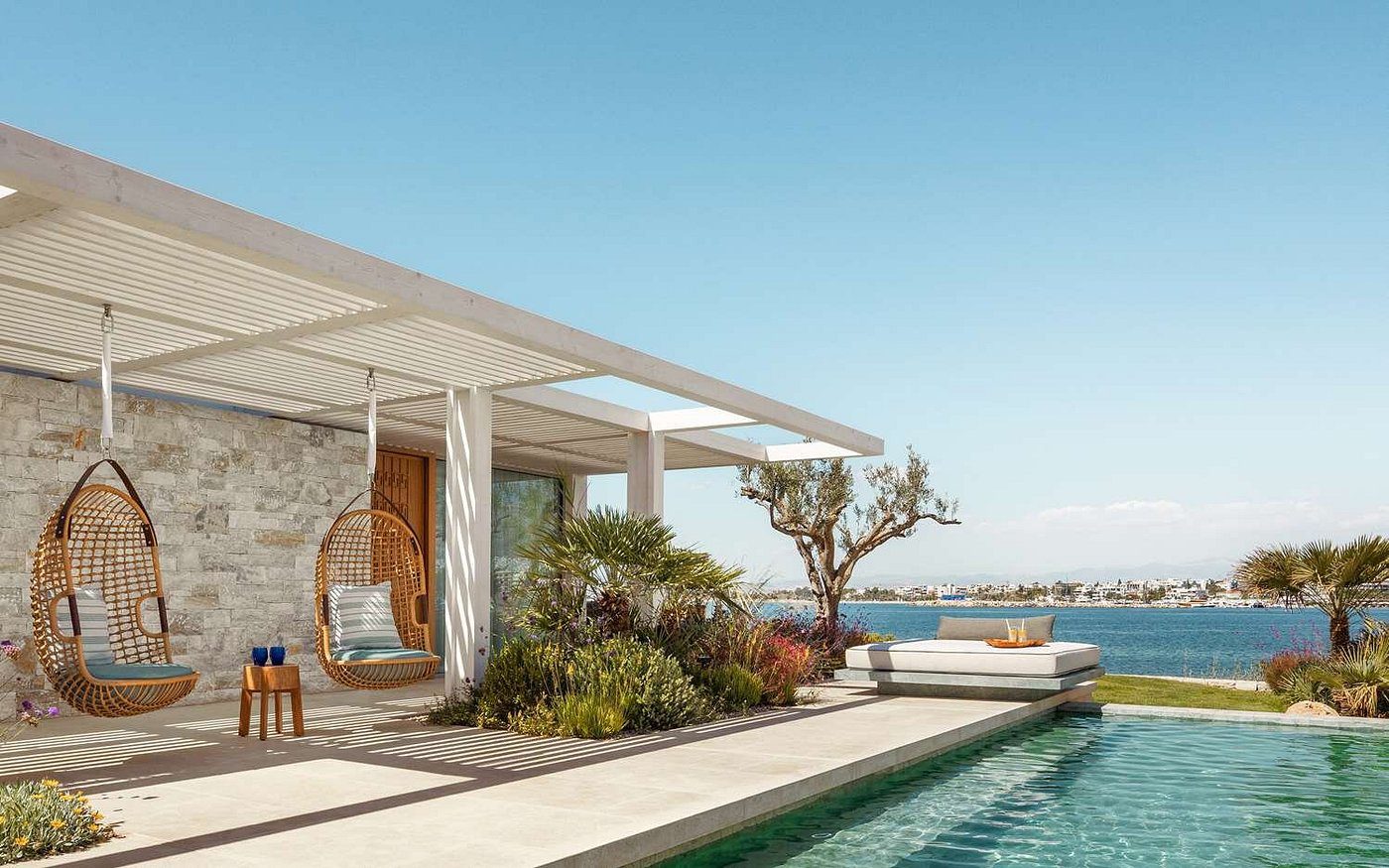 Modern poolside patio with greenery and ocean views under a clear sky.