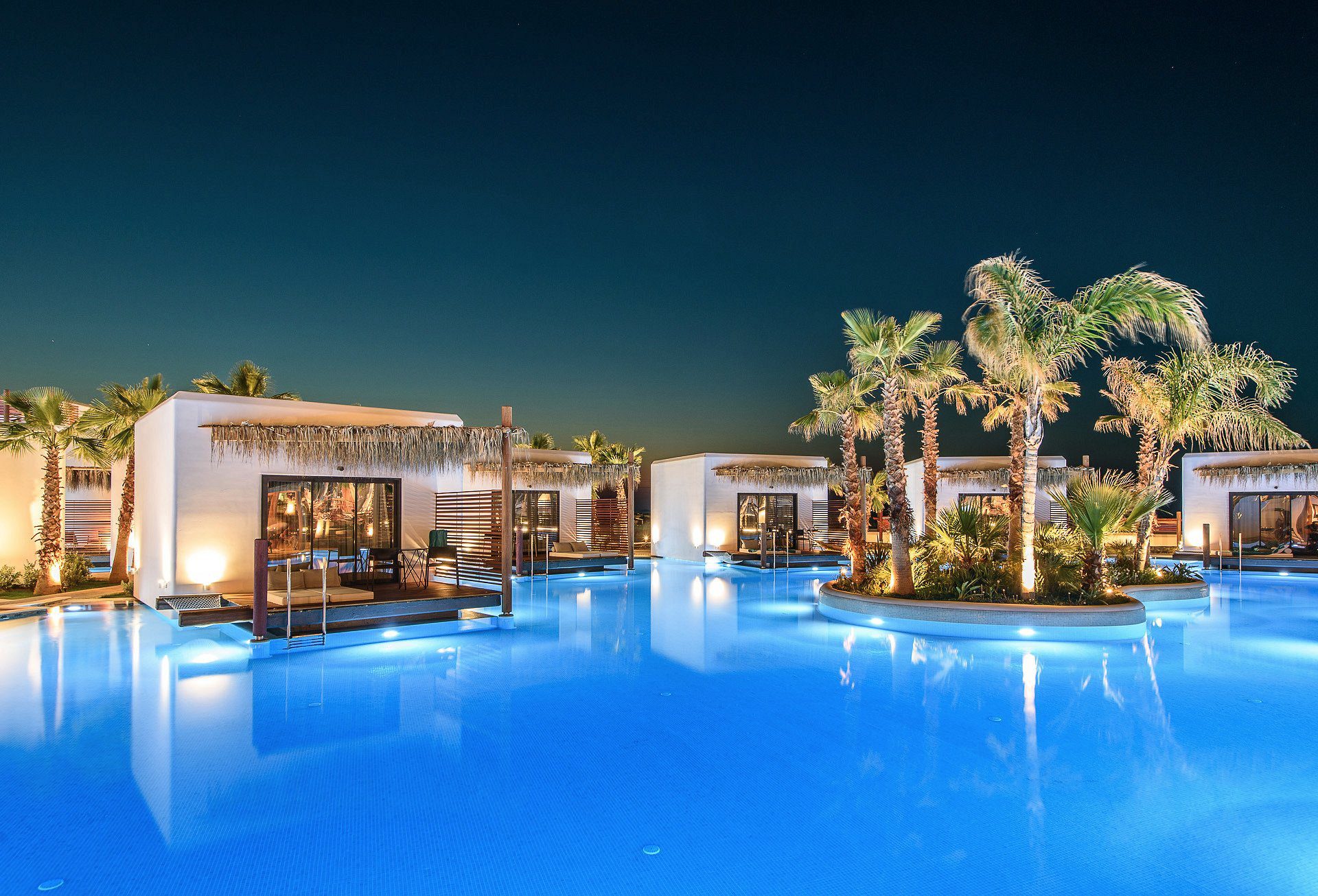 Luxurious resort pool area at night with illuminated water and modern cabanas.