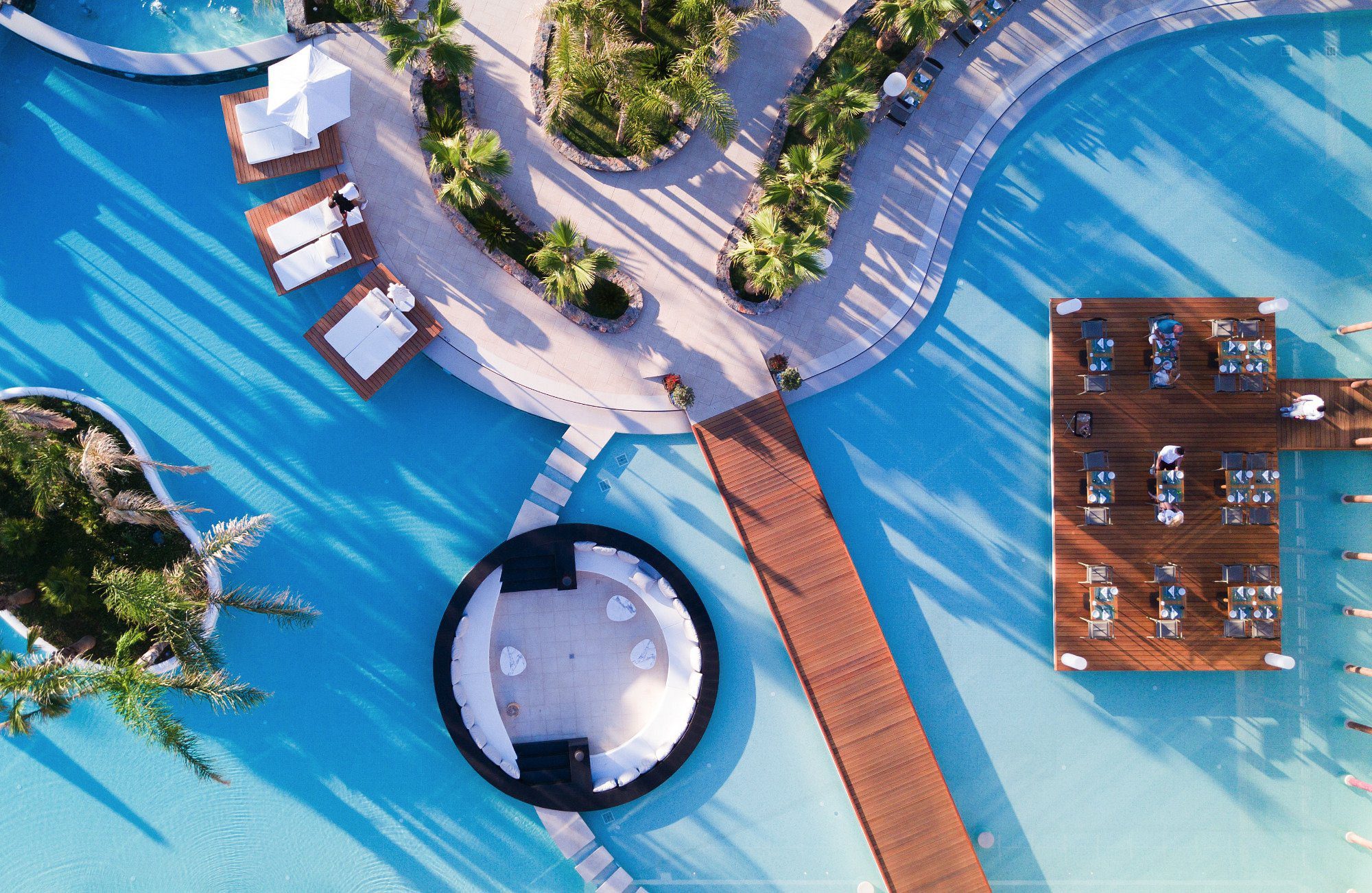 Aerial view of a luxurious pool area with a circular floating lounge and sunbeds.