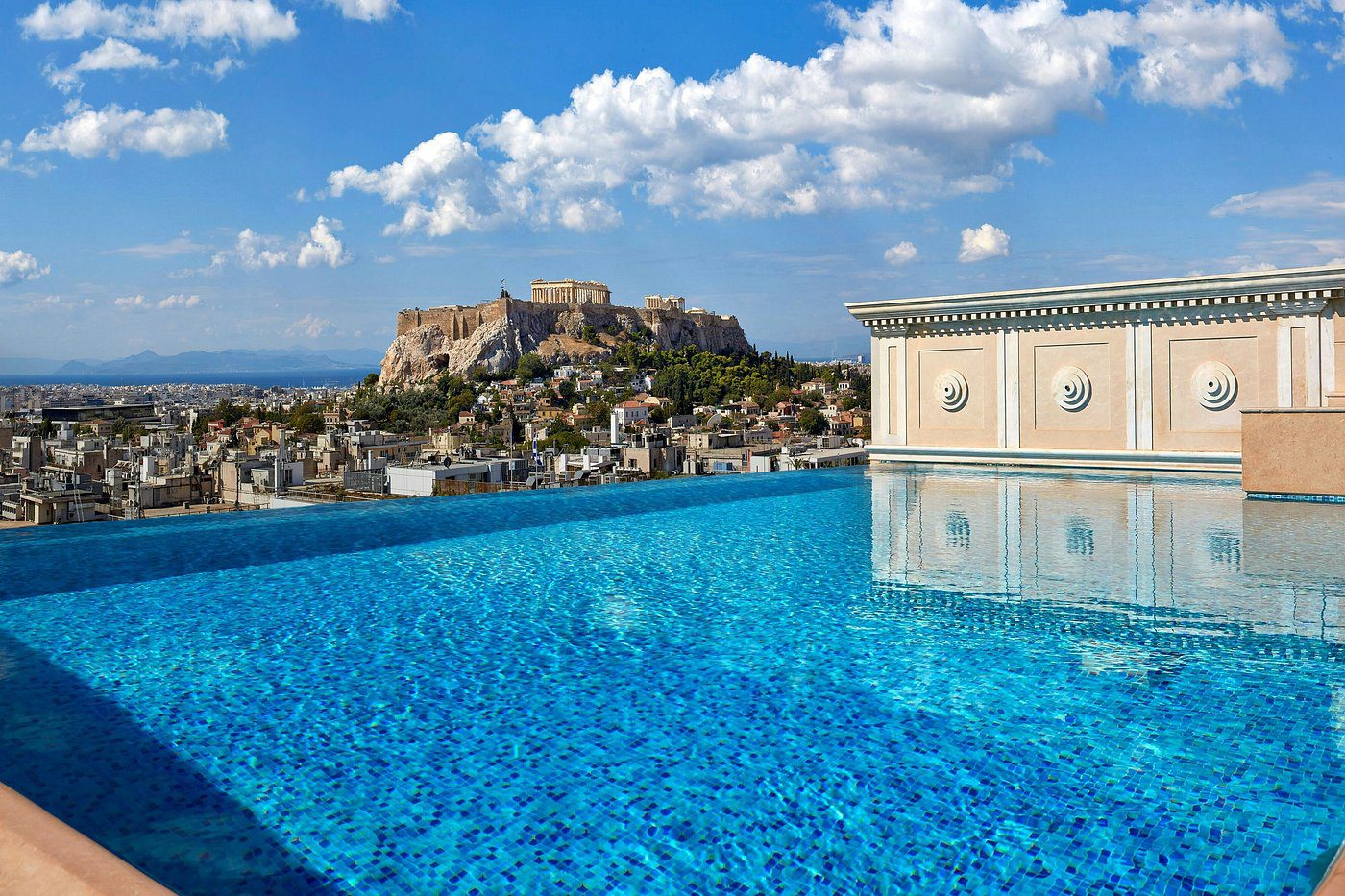 Infinity pool overlooking a historic hilltop fortress under a blue sky.