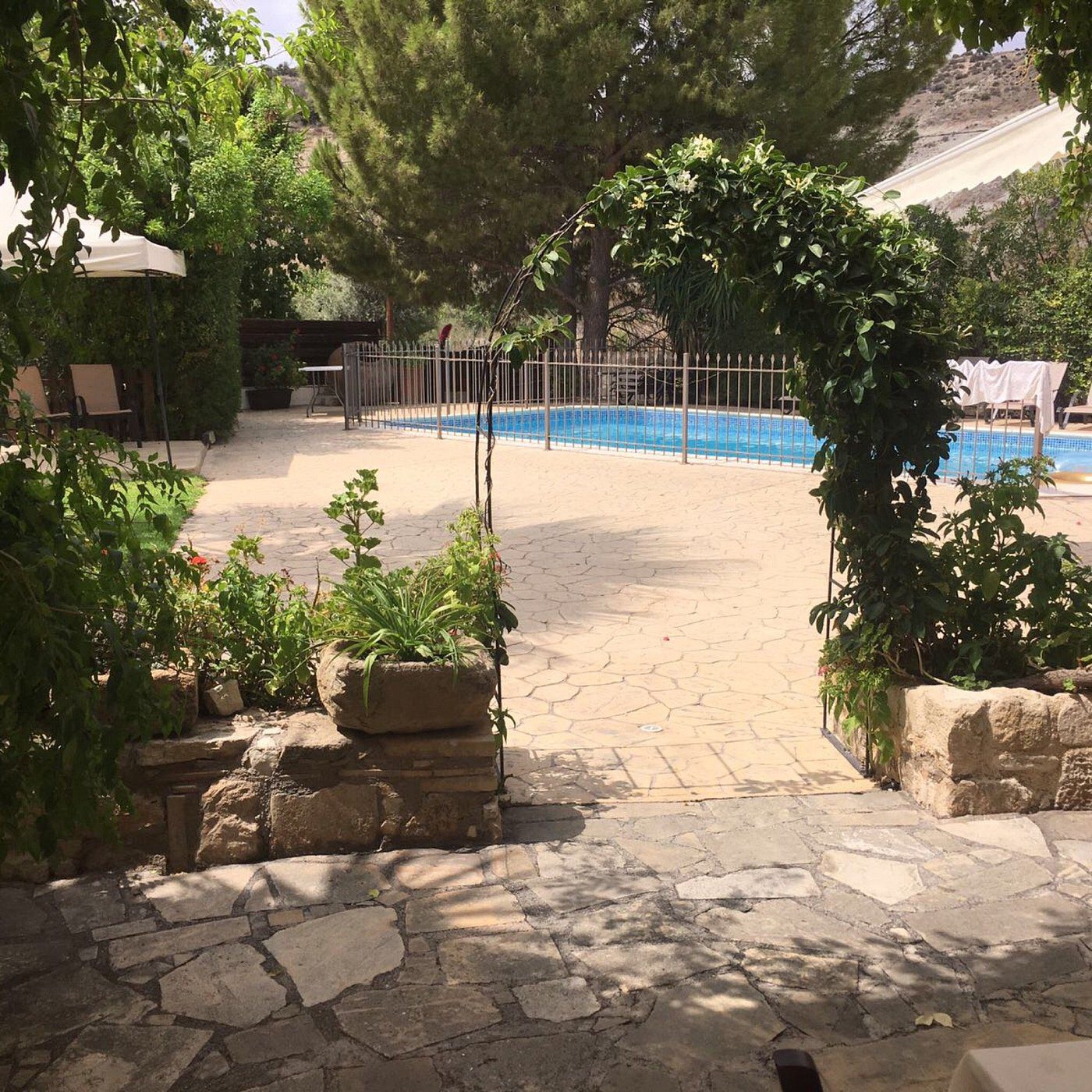 Stone pathway leading to a pool surrounded by greenery and an archway.