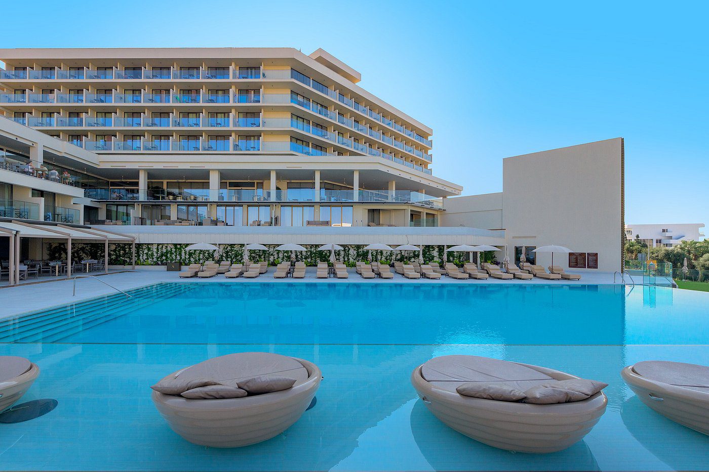 Modern resort with a large pool and round sun loungers under clear skies.