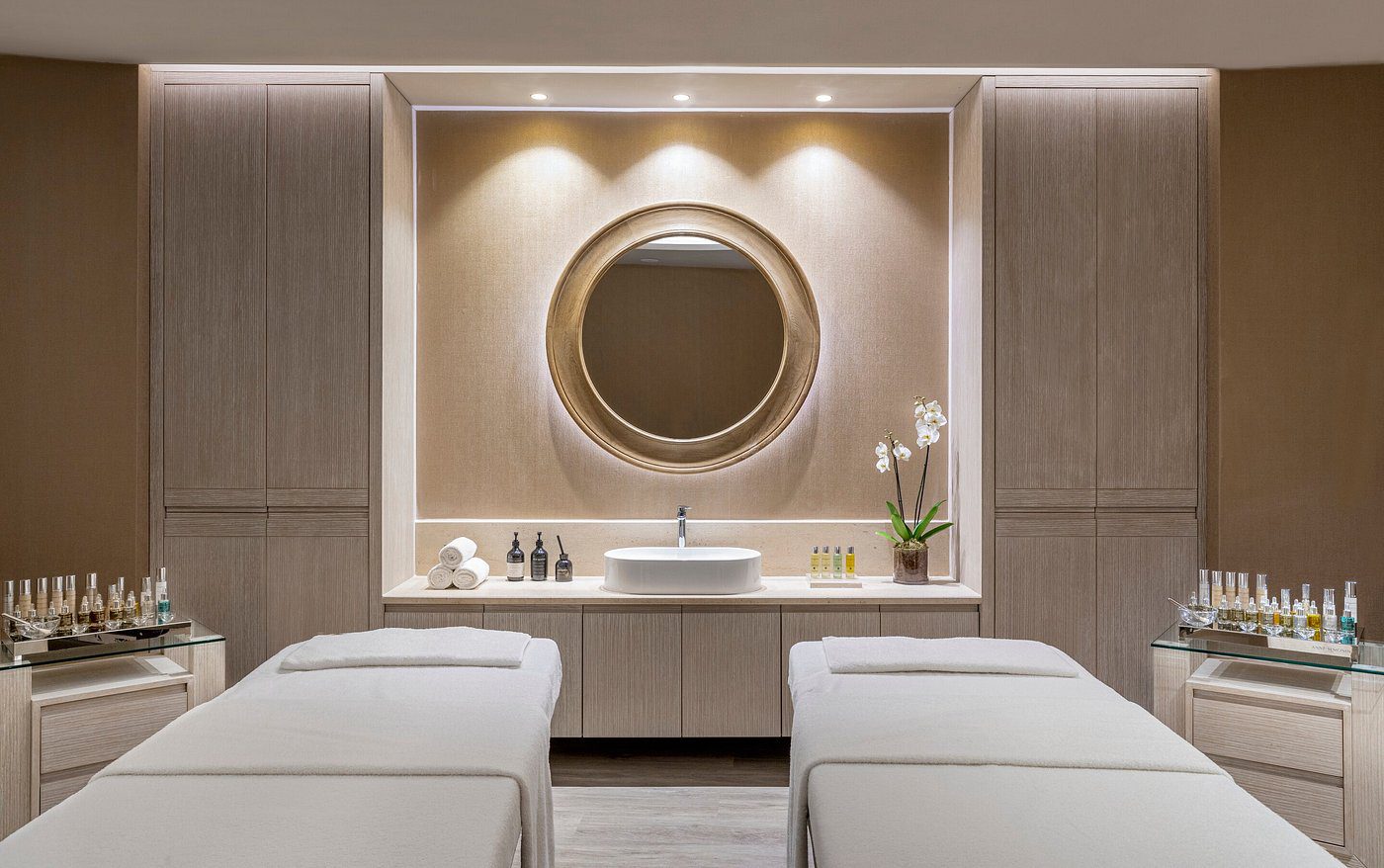 Elegant spa room with twin massage tables and round mirror.