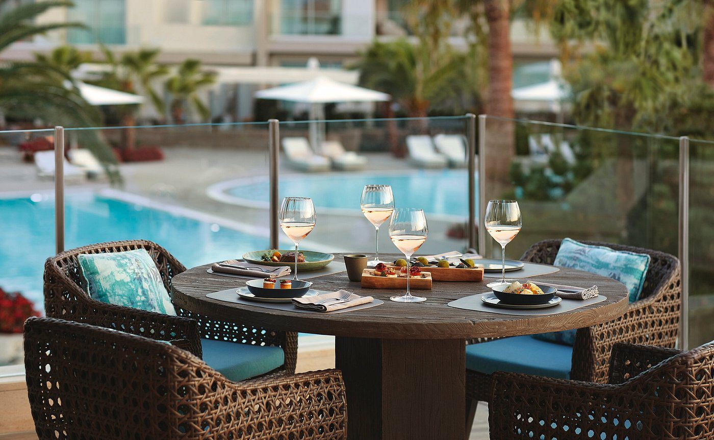Outdoor dining table set by a pool with snacks and drinks.