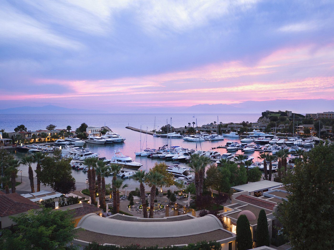 A tranquil marina at sunset with boats docked and a colorful sky.
