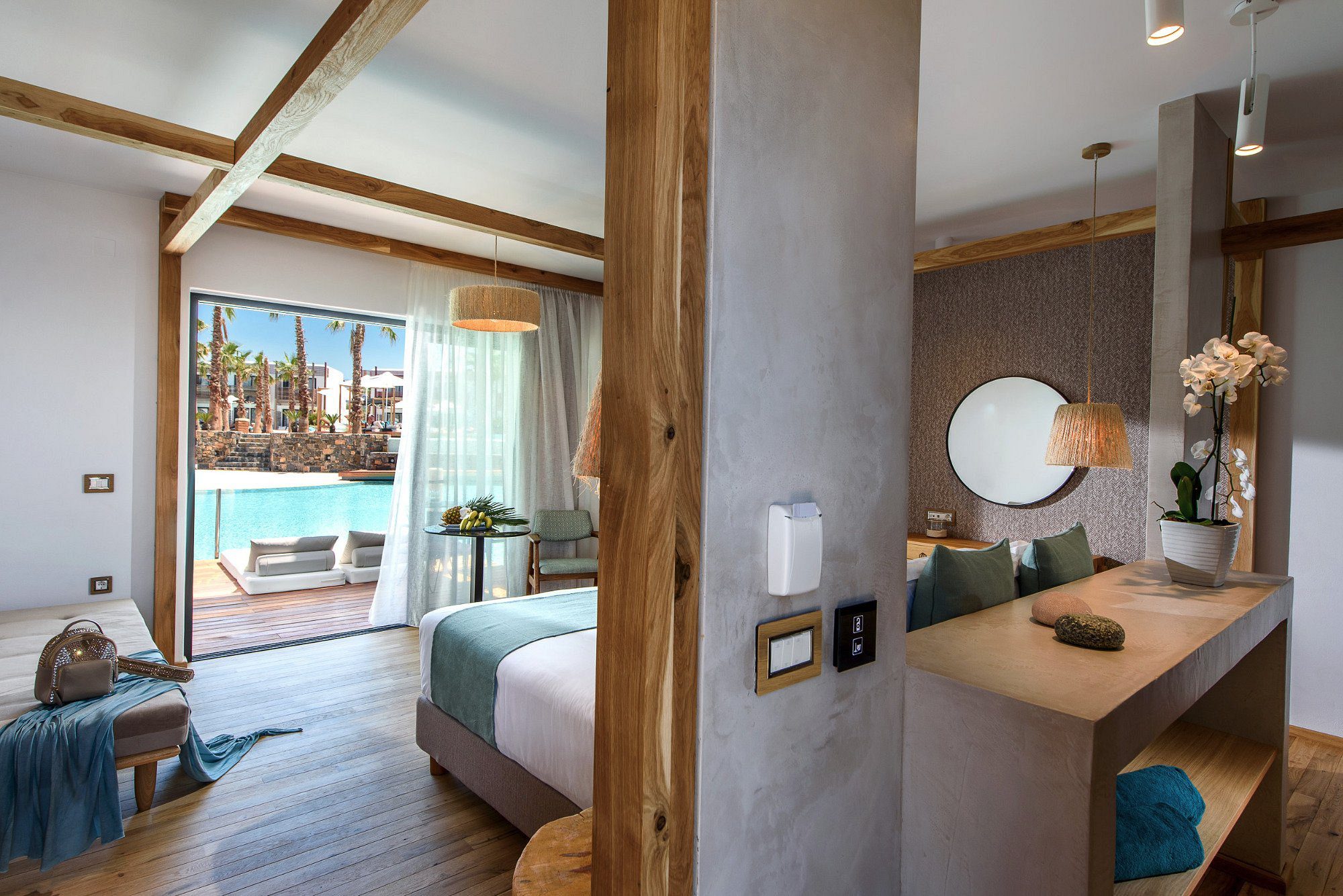 Modern bedroom and bathroom interior with wooden accents and a view of the pool.