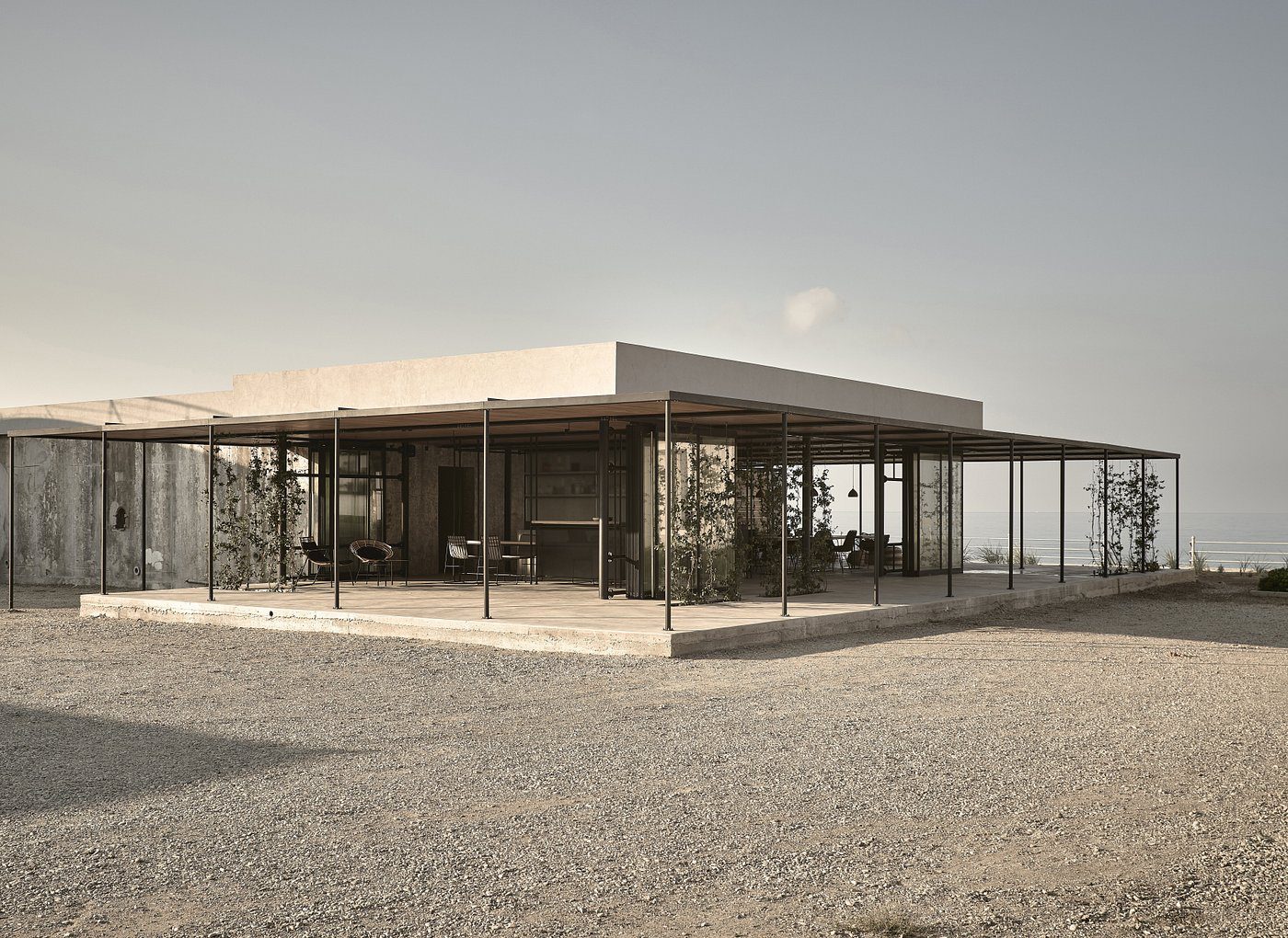A modern glass house with a flat roof in a barren landscape.