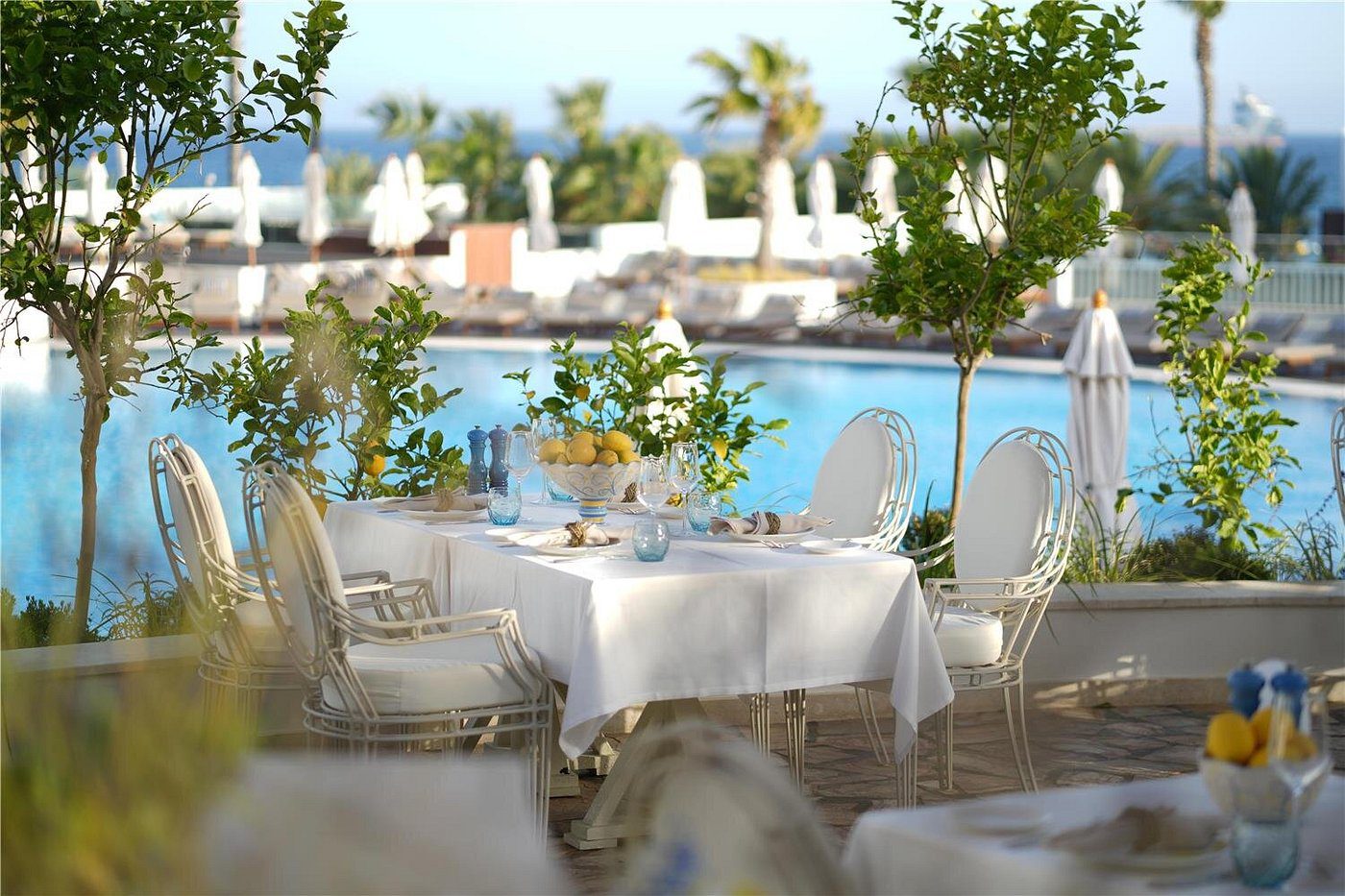 Elegant outdoor dining setup by the pool with white chairs and greenery.