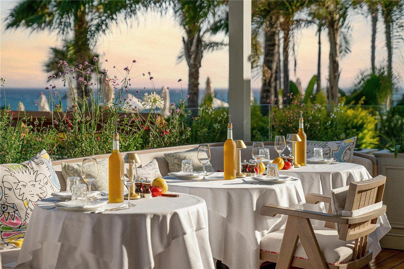 Elegant outdoor dining setup with white tablecloths and orange juice at sunset.