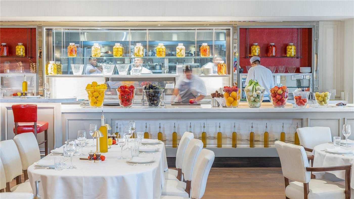 Elegant restaurant interior with white tables and a vibrant open kitchen.