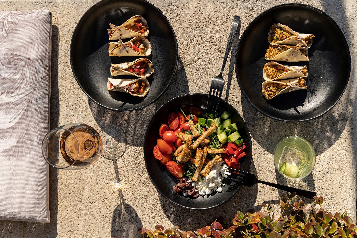 Three plates of tacos and a bowl of fresh salad on a table.