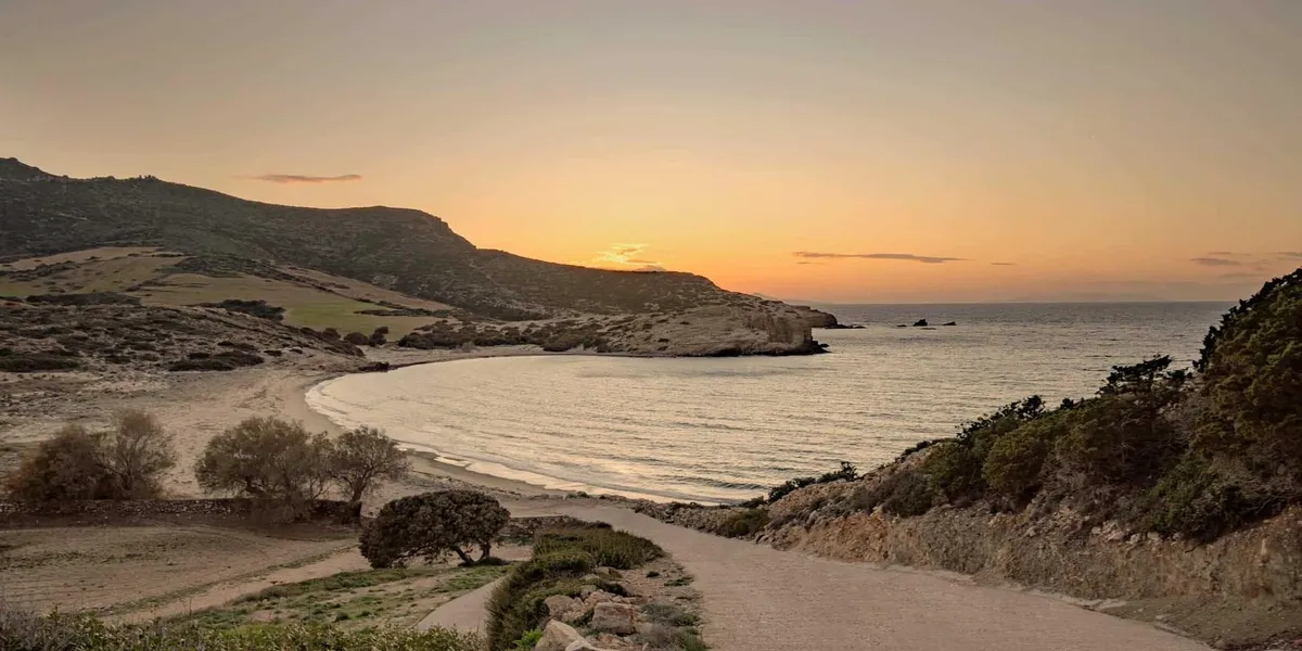 Sunset over a rocky coastline with gentle waves and a dirt path.