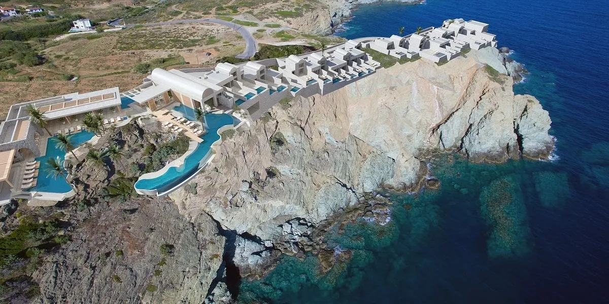 Cliffside resort with white buildings and a turquoise pool overlooking the sea.