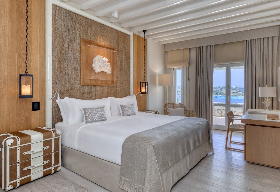 Modern bedroom with neutral tones and a large window overlooking the sea.