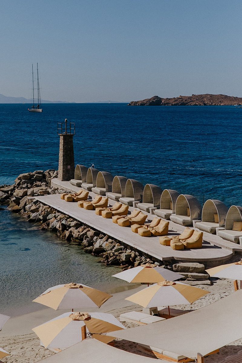 A calm sea with a stone pier and a lighthouse under a clear sky.