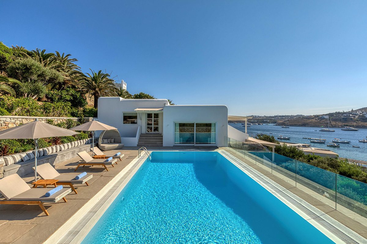 Modern villa with a pristine pool and stunning sea views under a clear blue sky.