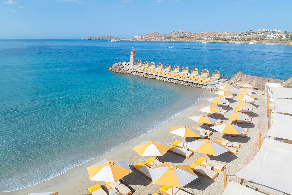 Sunny beach with yellow and white umbrellas by clear blue water.