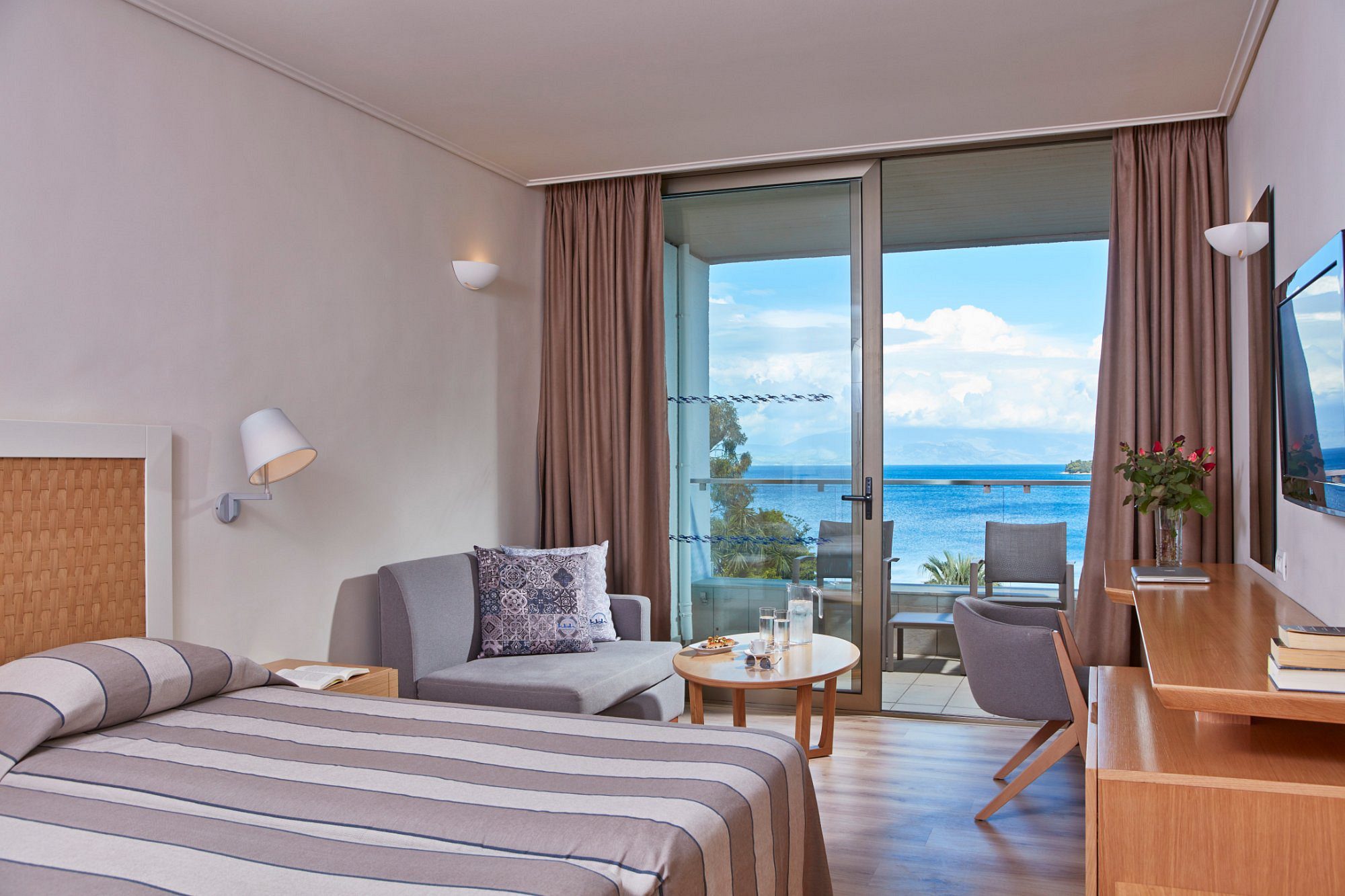 Modern hotel room with sea view and balcony seating.