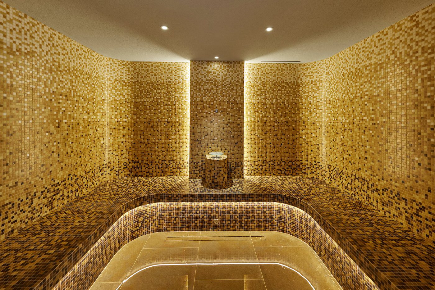 Luxurious golden mosaic steam room with curved seating and ambient lighting.