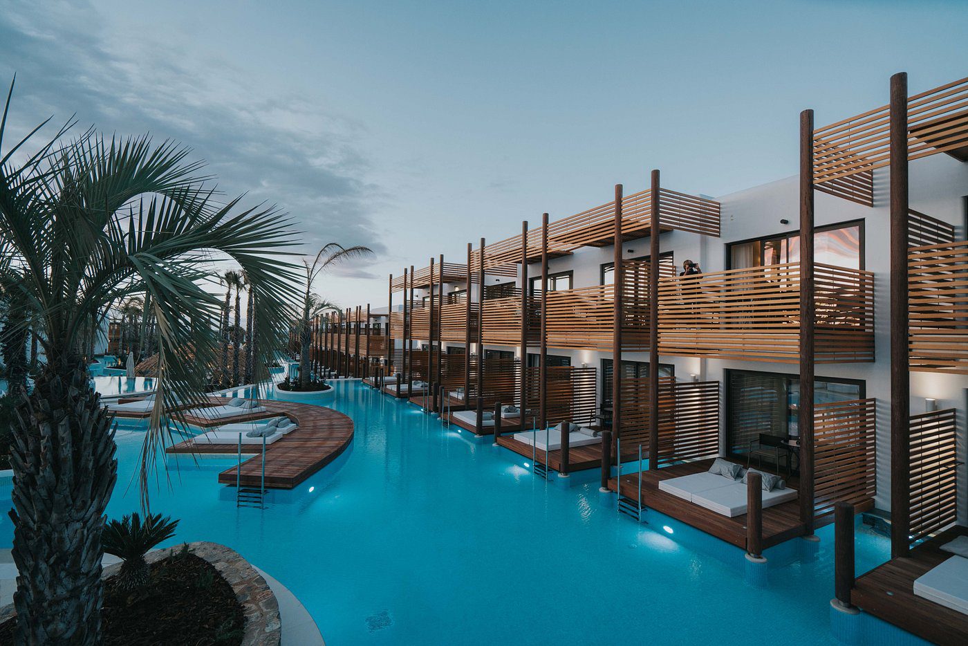 Modern resort pool area with wooden cabanas and lounge chairs at sunset.