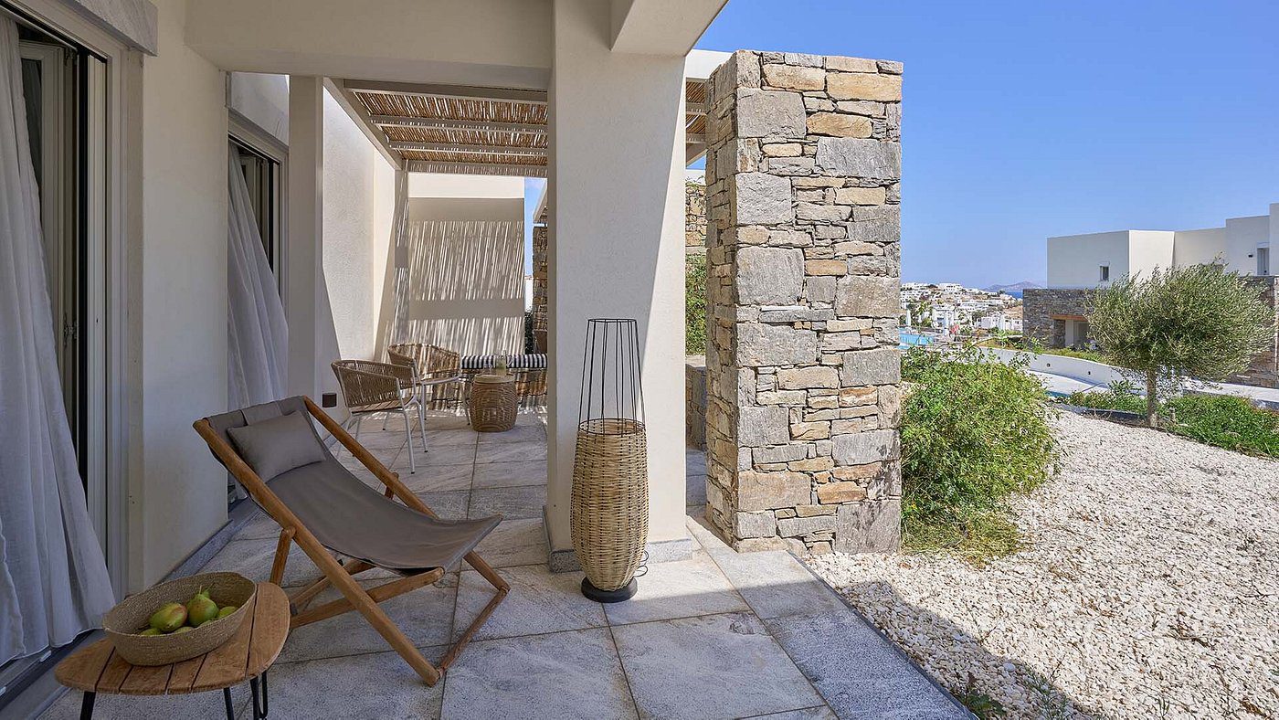 Sunny outdoor lounge area with stone wall and wooden deck chair.