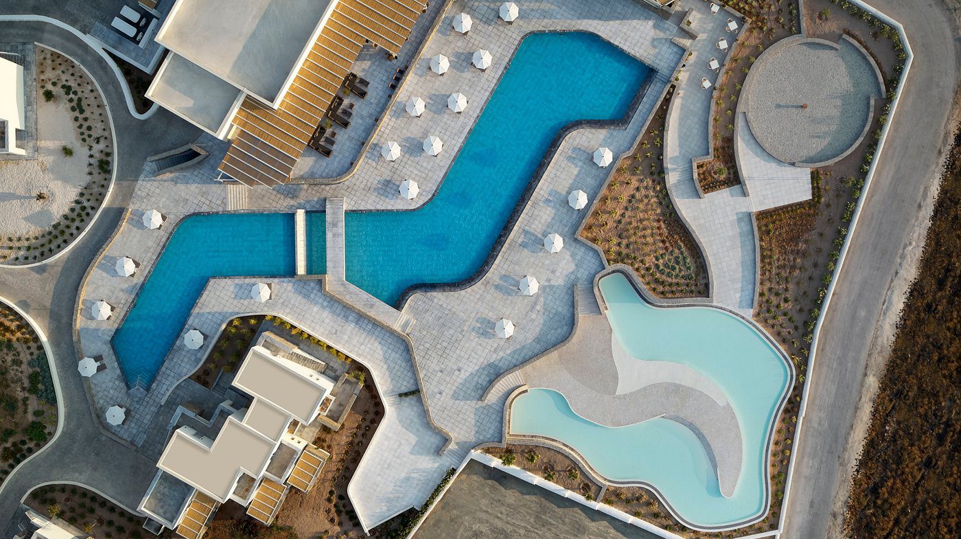 Aerial view of a stylish resort pool area with modern lounge chairs and adjacent buildings.