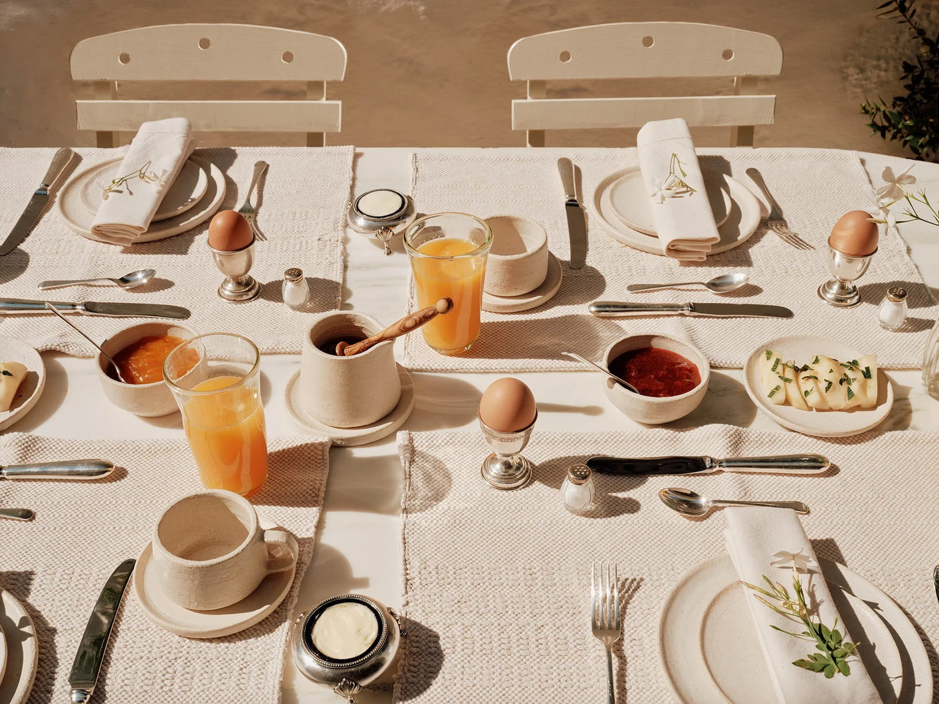 Elegant breakfast table set with juice, coffee, and pastries in warm sunlight.