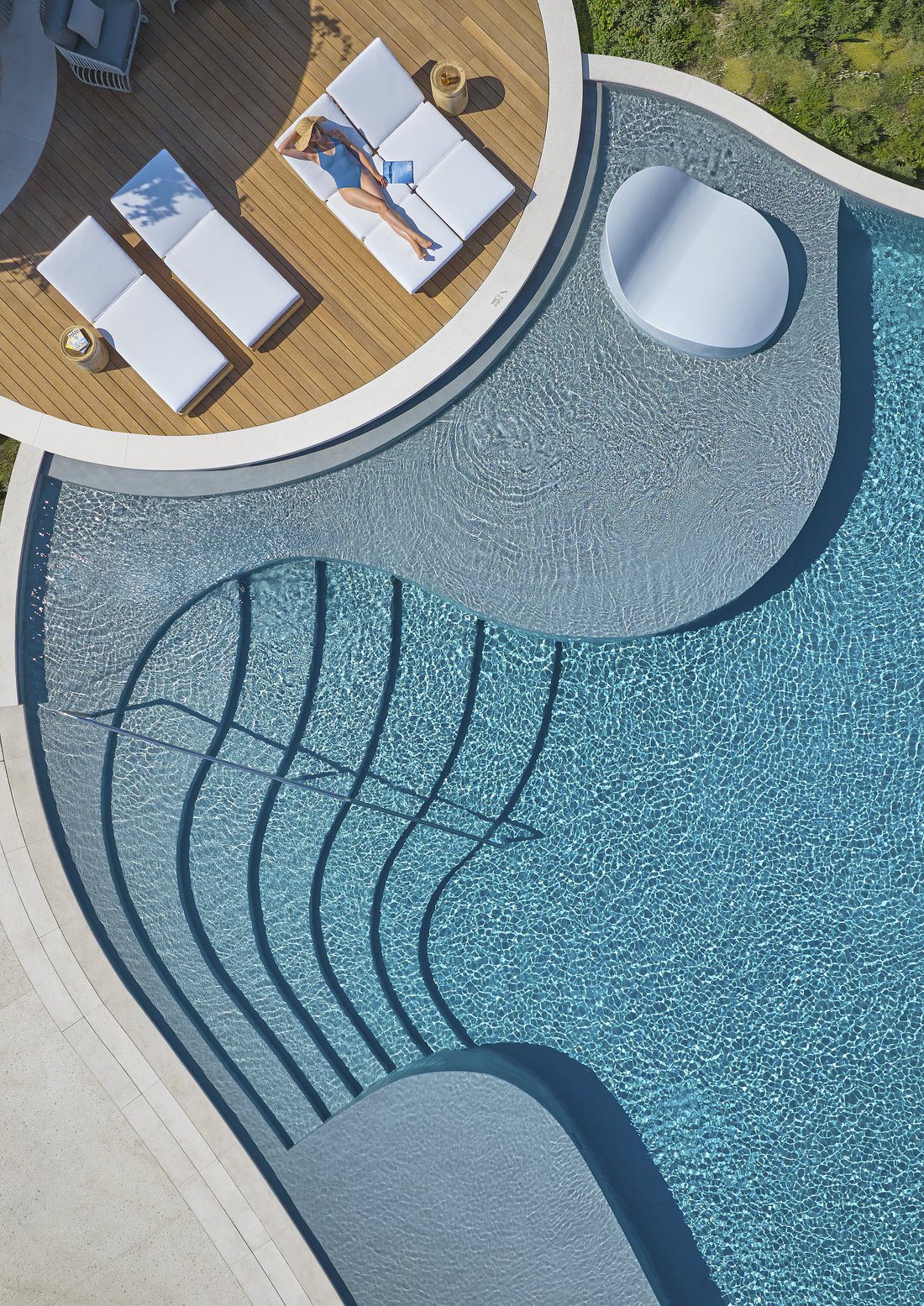 Curved steps lead into a clear blue swimming pool with a nearby seating area.