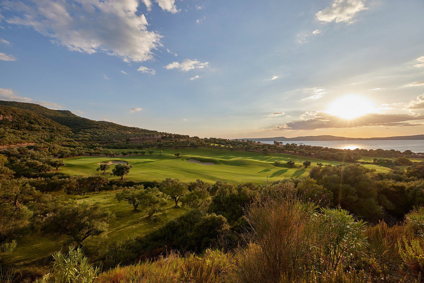 Scenic golf course under a bright blue sky with clouds at sunset.