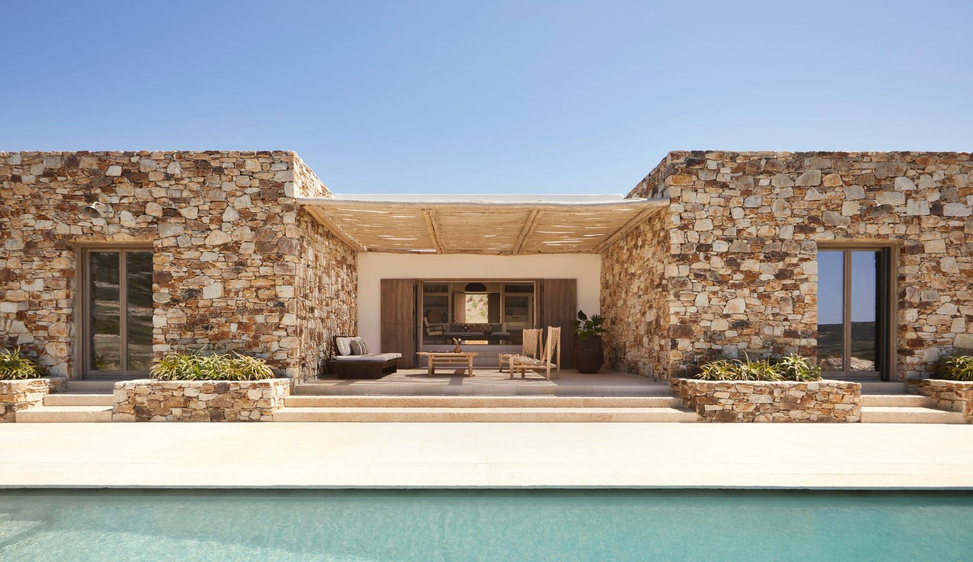 Modern stone house with a pool and outdoor seating area.