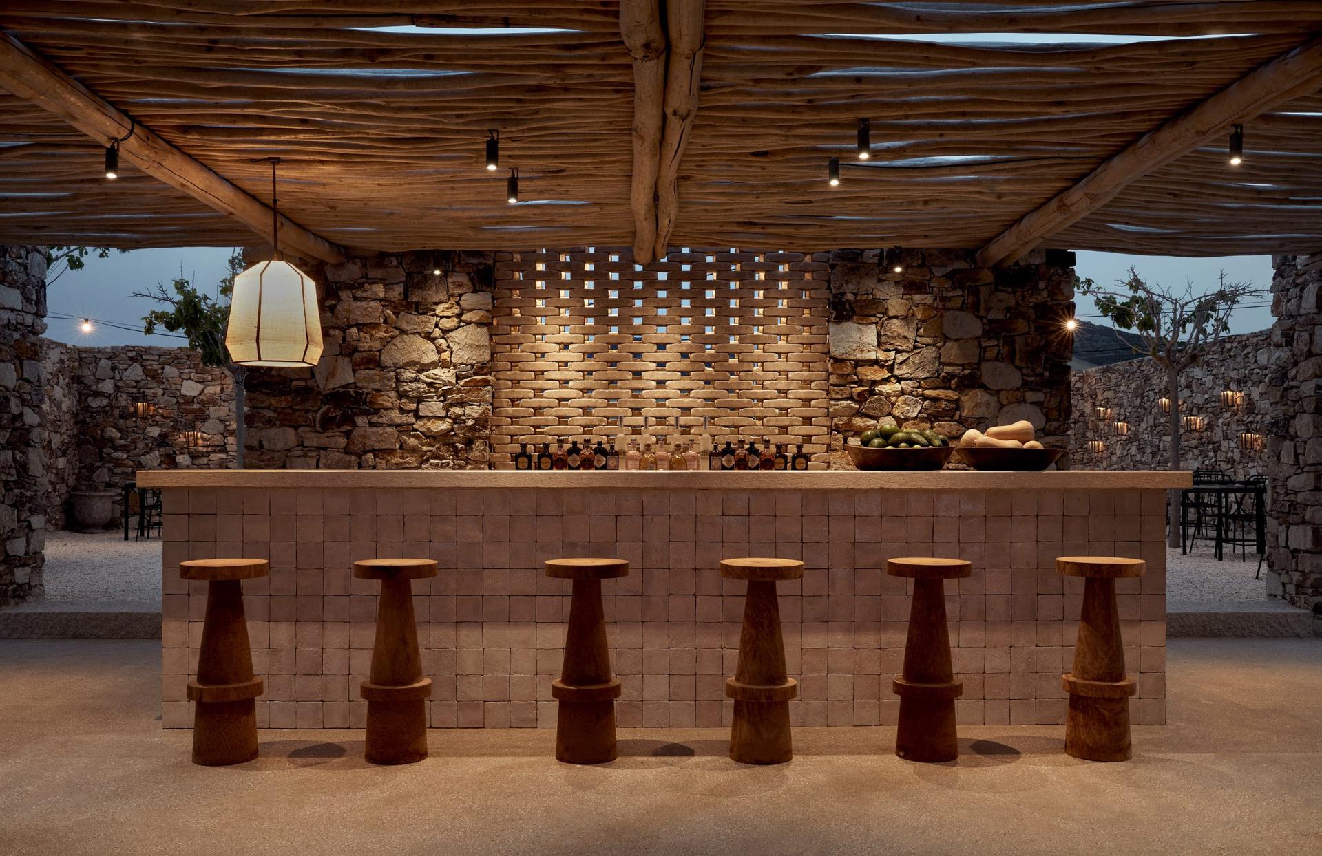 Rustic bar with wooden stools and stone walls under warm lighting.