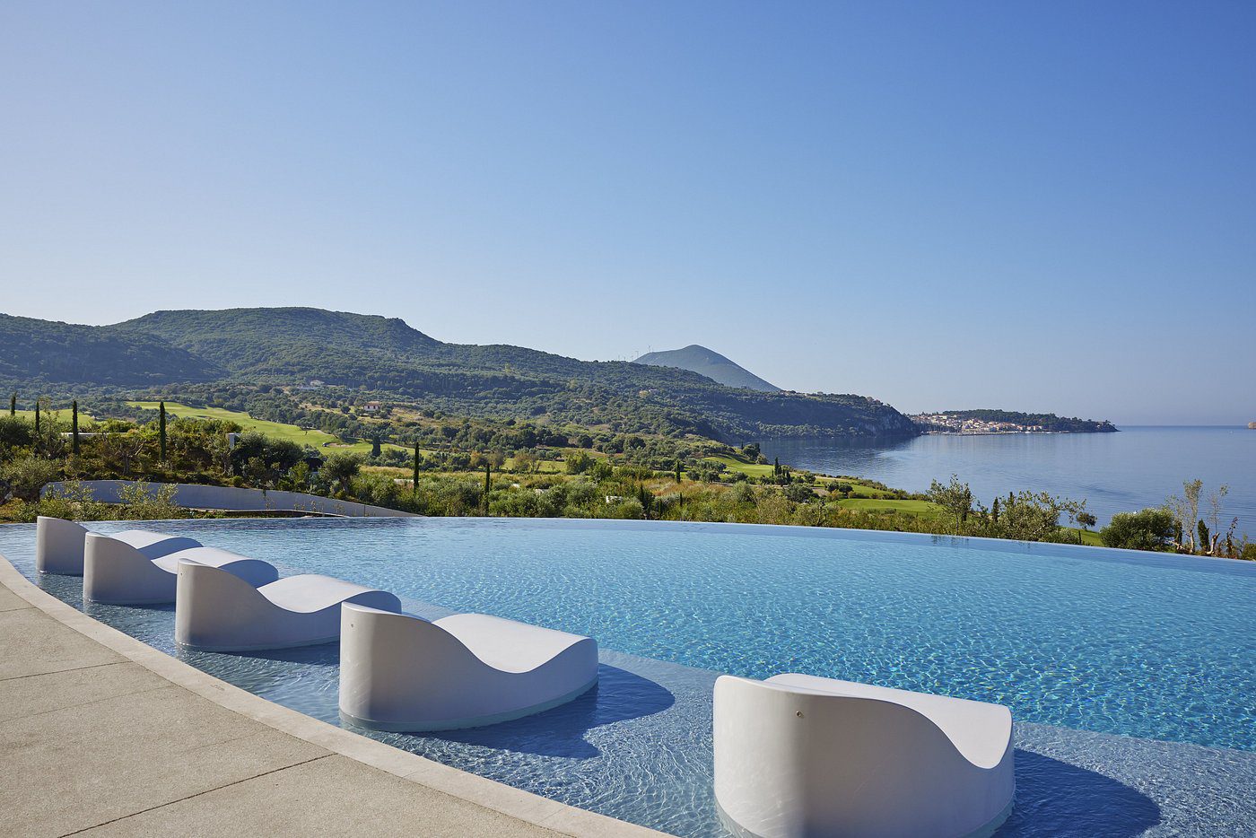 Infinity pool overlooking lush green hills and a clear blue sky.