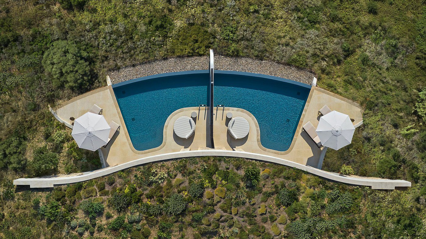 Aerial view of a modern curved pool with lounge chairs surrounded by greenery.