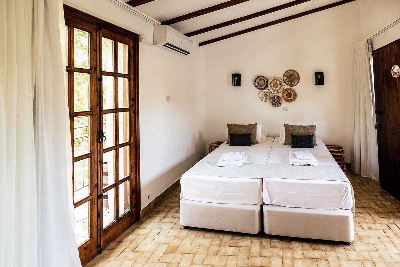 Minimalist bedroom with twin beds and natural light from wooden framed doors.
