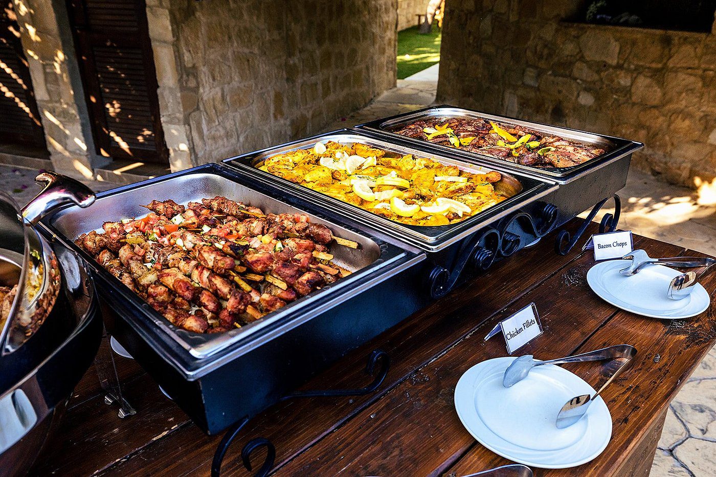 Buffet trays with roasted potatoes and baked dishes on wooden table.