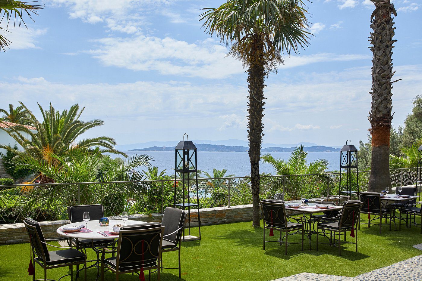 Outdoor dining area with palm trees overlooking the sea.
