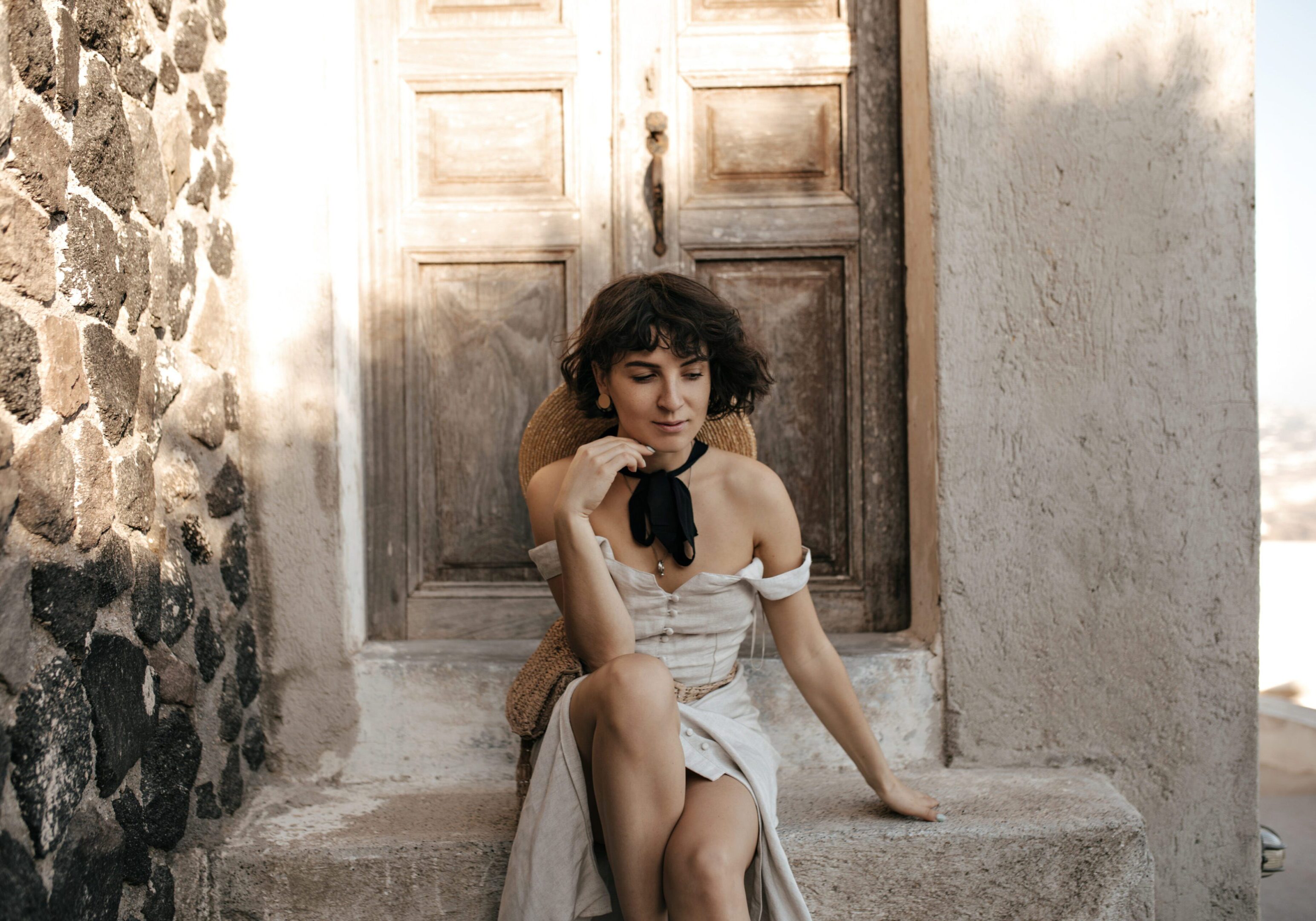 A woman in a white dress sits on stone steps in front of a wooden door.