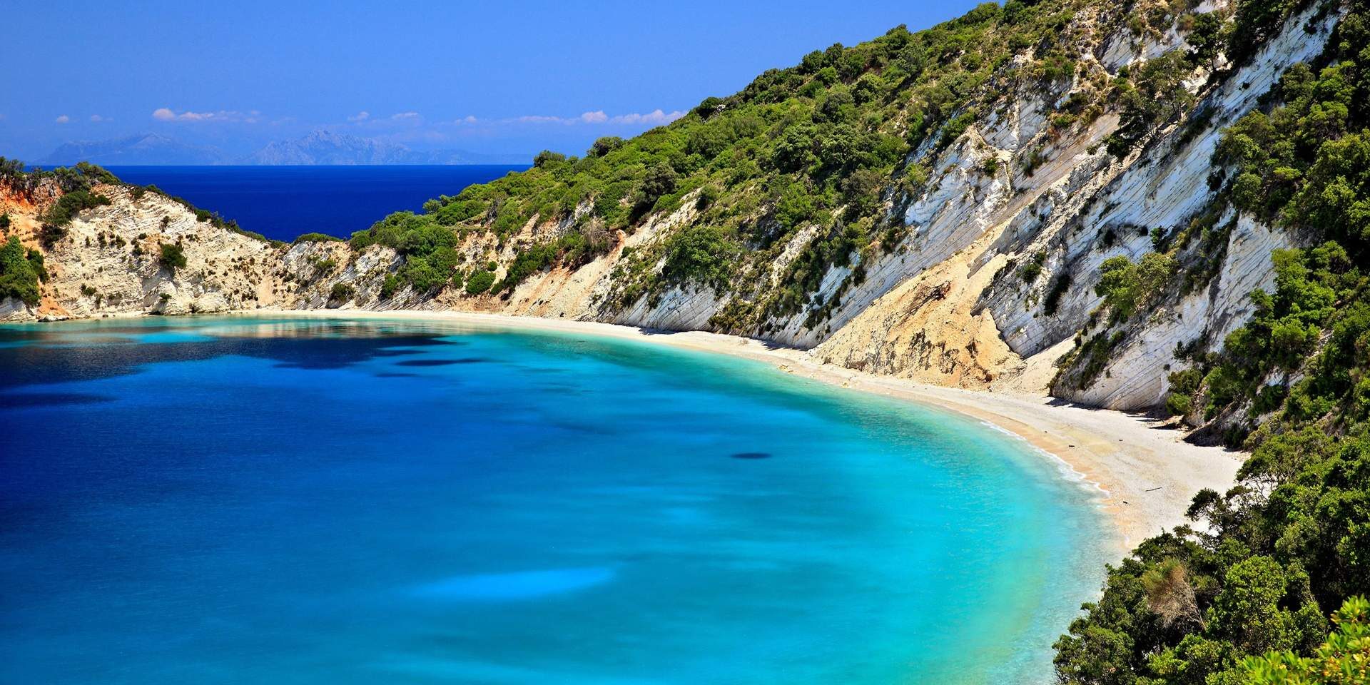 A serene beach with turquoise waters and lush green cliffs.