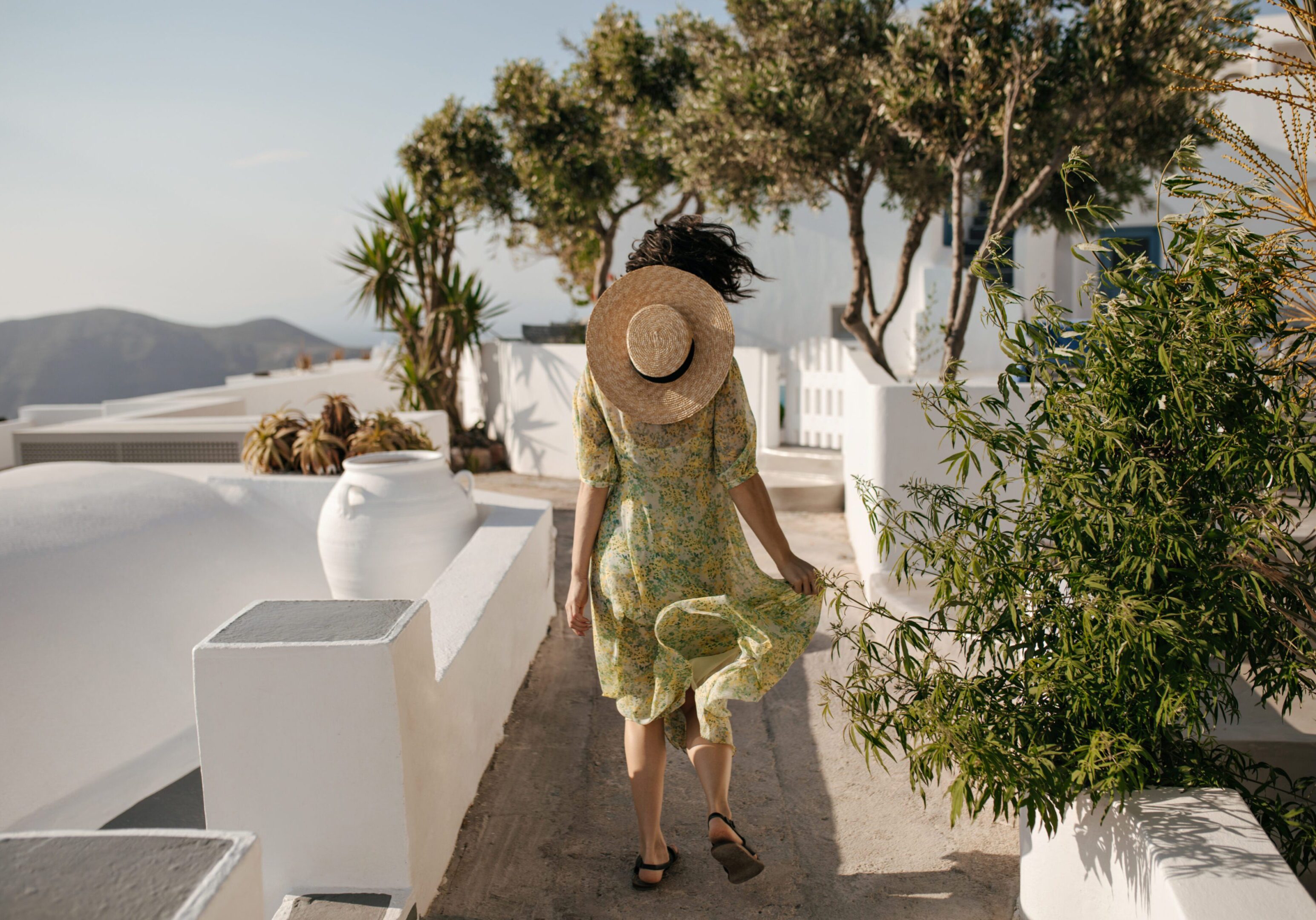 Woman in green dress and hat walking outdoors on a sunny day.